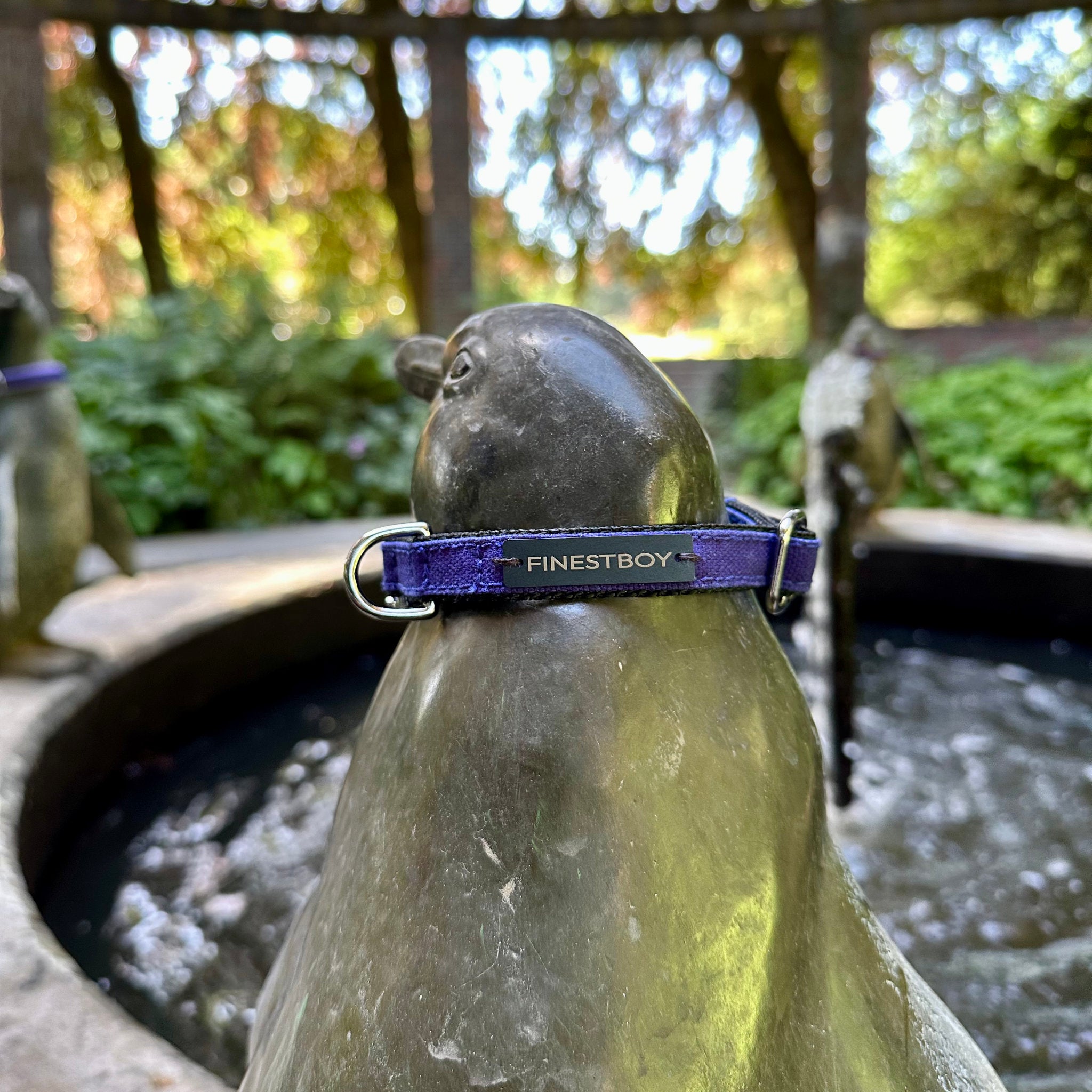 Pinguin trägt FINESTBOY-Halsband, 15mm, schwarzes Gurtband mit royalblauem Canvas-Streifen und verchromten Vollmessing-Applikationen und verchromter Metallsteckschnalle, im Hamburger Stadtpark an einer Pinguin-Skulptur