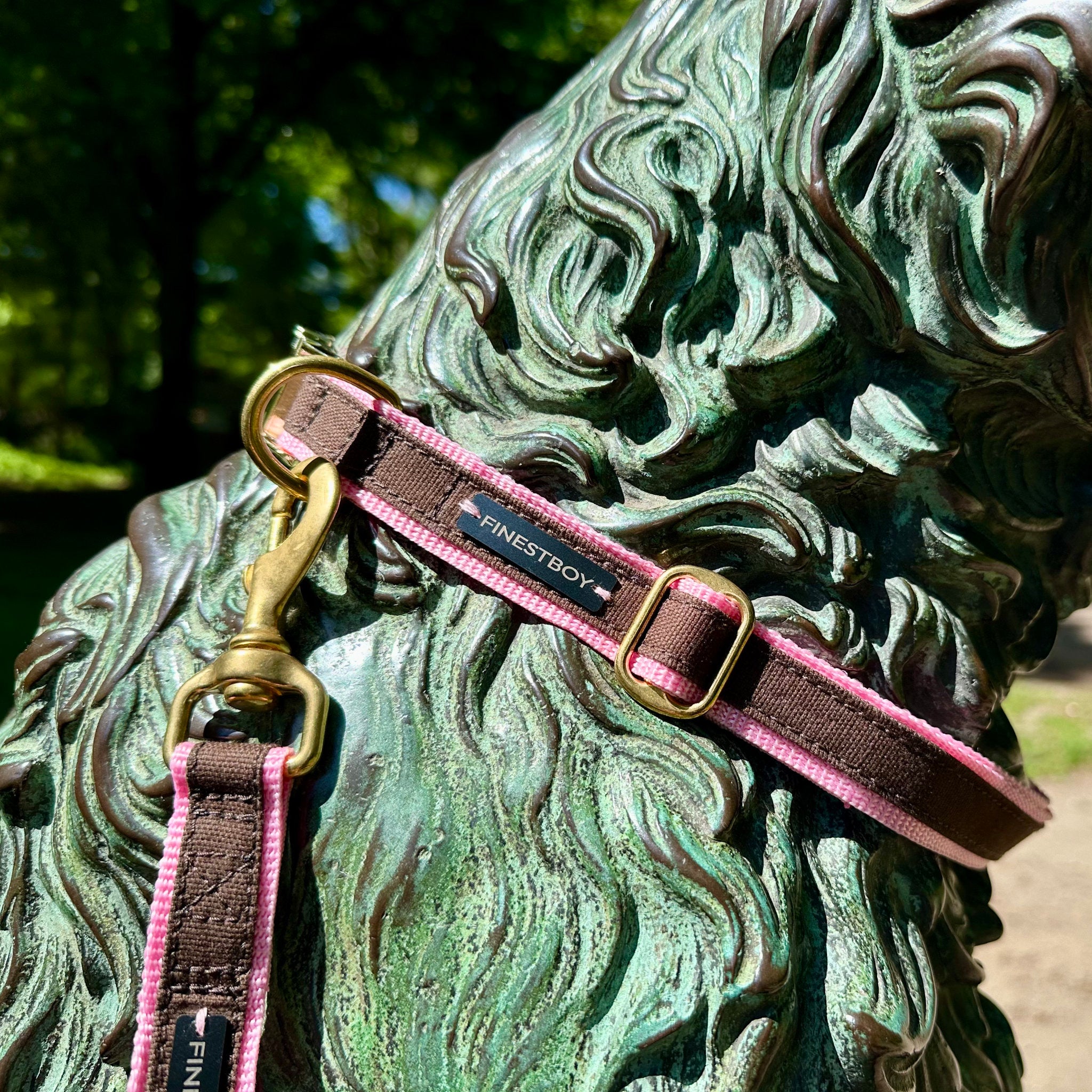 Hund trägt FINESTBOY-Bundle aus Halsband und Leine, 25mm, rosafarbenes Gurtband mit dunkelbraunem Canvas-Streifen und Vollmessing-Applikationen, vermessingter Metallsteckschnalle und Vollmessing-Karabiner, im Hamburger Stadtpark an einer Hundeskulptur