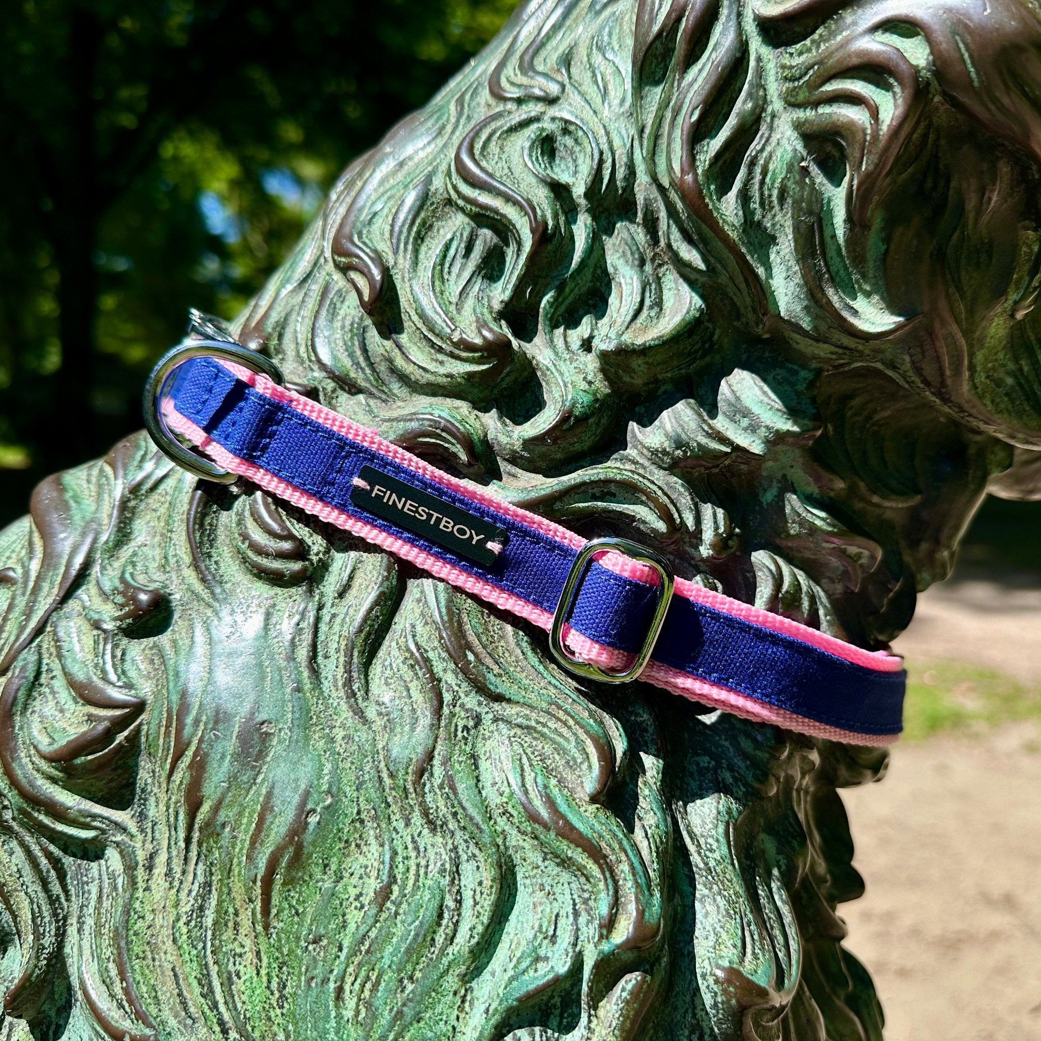 Hund trägt FINESTBOY-Halsband, 25mm, rosafarbenes Gurtband mit royalblauem Canvas-Streifen und verchromten Vollmessing-Applikationen und verchromter Metallsteckschnalle, Nahaufnahme im Hamburger Stadtpark an einer Hundeskulptur